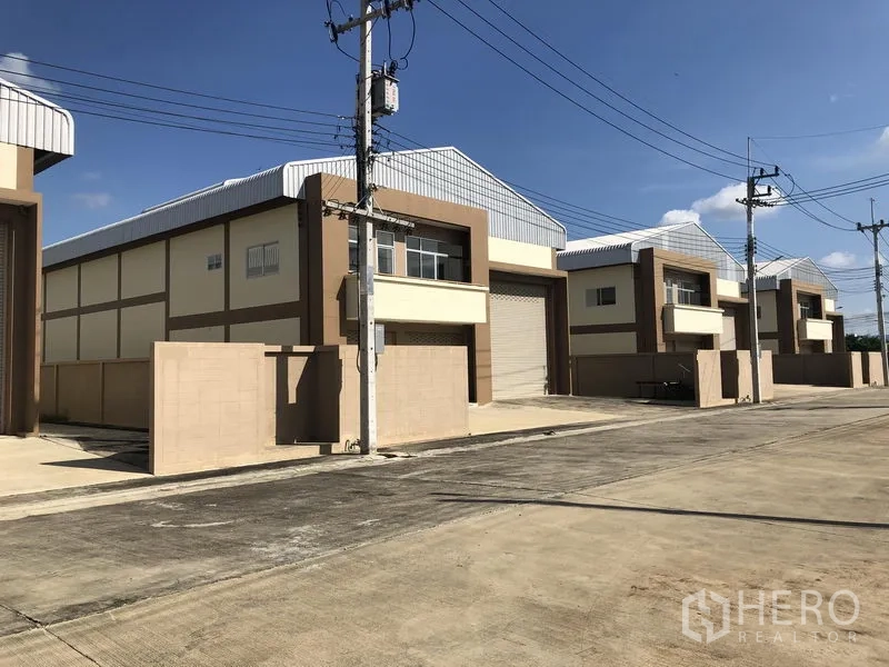 工厂 出租或出售在Pathum Thani - 多座同款仓库沿宽阔园区道路排列，设电线杆与前方围墙。