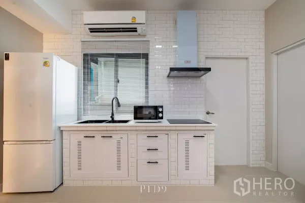 Townhouse for rent in Bang Phli, Samut Prakan - White subway‑tile kitchen with window, sink, cooktop, hood and refrigerator