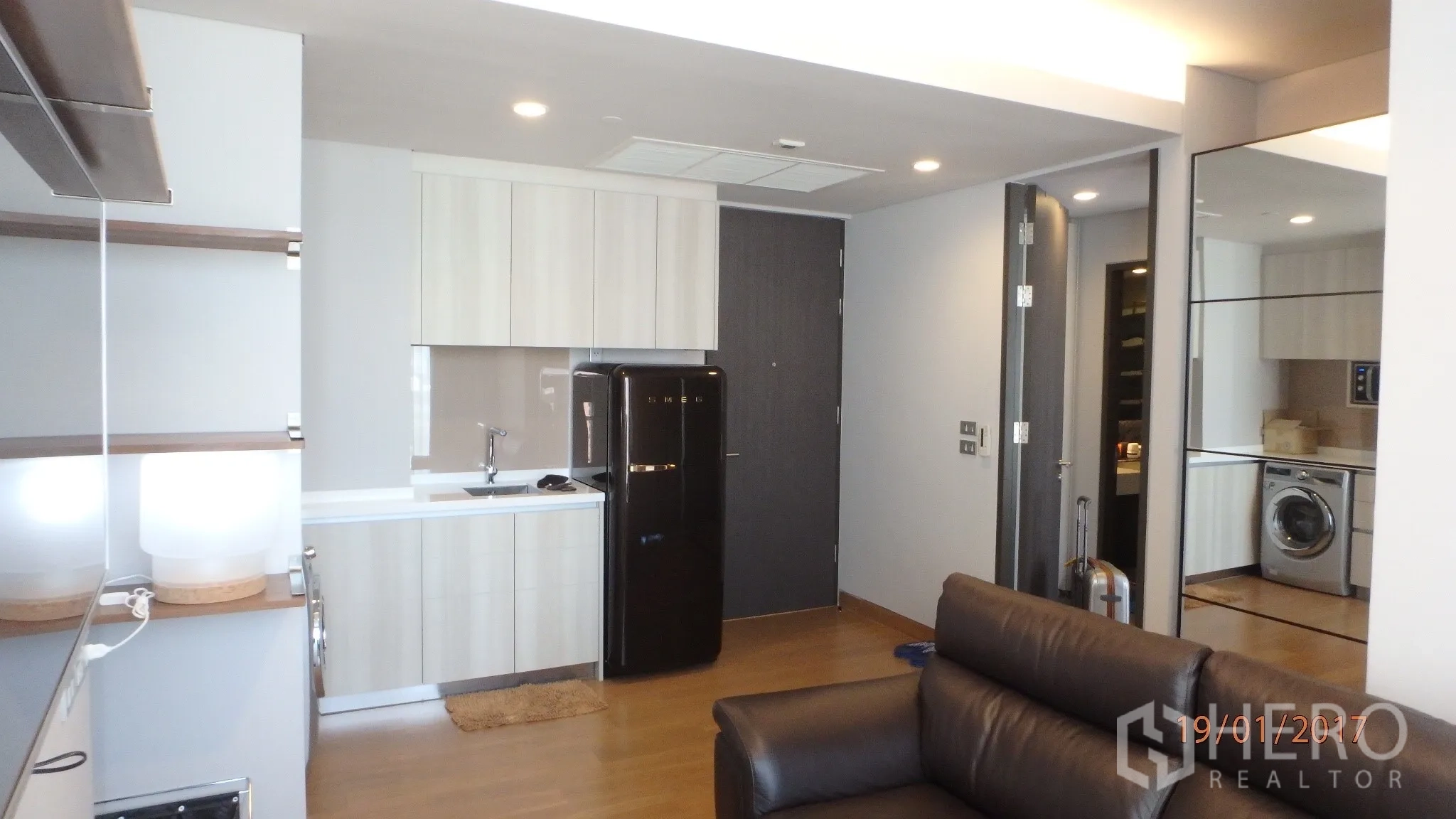 คอนโด ให้เช่าในKhlong Toei, Bangkok - ครัวแพนทรีตู้ลอยสีอ่อน ตู้เย็นสีดำ อ่างล้าง และไฟดาวน์ไลท์ เชื่อมต่อพื้นที่นั่งเล่น