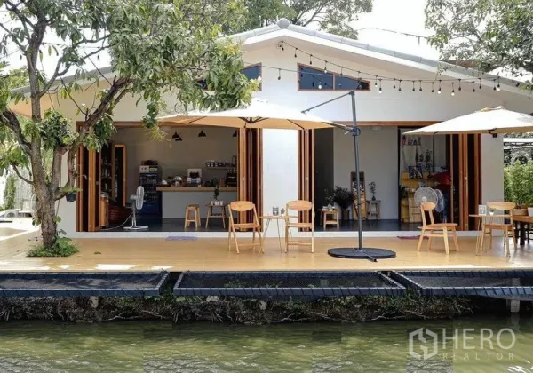 零售空间 出租在Suan Luang, Bangkok - 临河立面，开放式咖啡吧台，宽幅折叠门、木平台与遮阳伞。