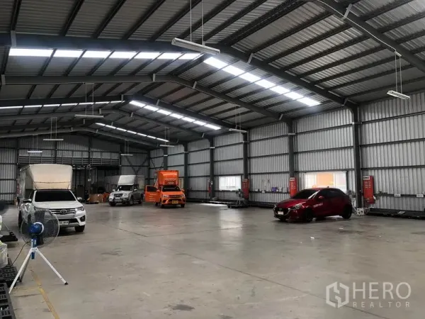 Warehouse for rent in Don Mueang, Bangkok - Warehouse bay with trucks and cars parked under skylight panels and LED lights.