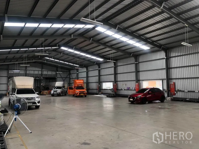 Warehouse for rent in Don Mueang, Bangkok - Warehouse bay with trucks and cars parked under skylight panels and LED lights.