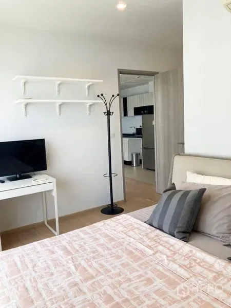 Condominium for rent in Watthana, Bangkok - Bedroom with bed, desk and wall shelves facing the doorway to the kitchen.