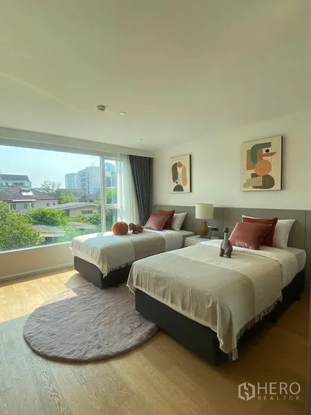 Condominium for rent in Watthana, Bangkok - Sunny twin bedroom with large window facing greenery and low-rise buildings.