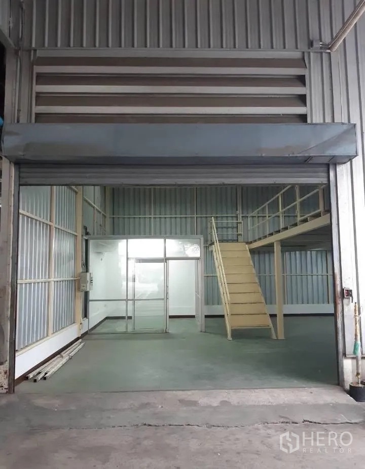 Warehouse for rent in Bang Kho Laem, Bangkok - Entrance with large roll-up shutter opening to the warehouse with office and stairs visible.