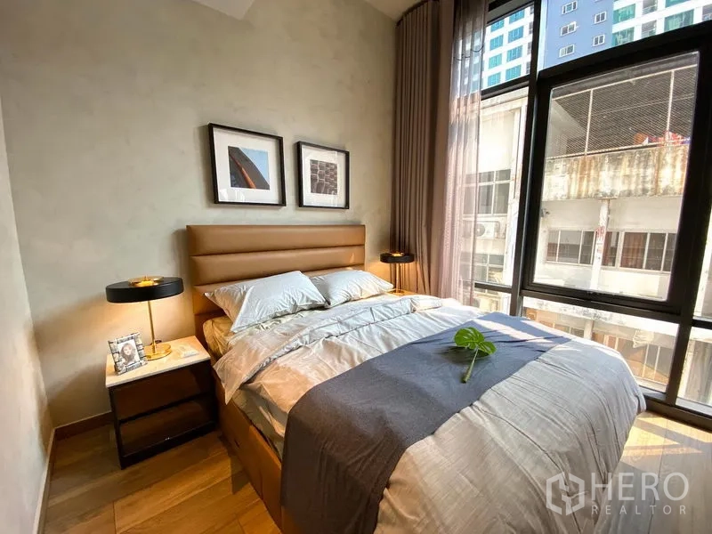 Condominium for rent in Watthana, Bangkok - Second bedroom with large windows, tan headboard, bedside tables, and urban outlook.