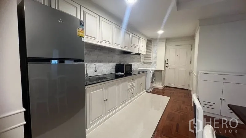 คอนโด ให้เช่าในWatthana, Bangkok - ครัวแบบแกลลีย์ตู้สีขาว ผนังลายหินอ่อน มีเตาไฟฟ้า ตู้เย็น และเครื่องซักผ้า