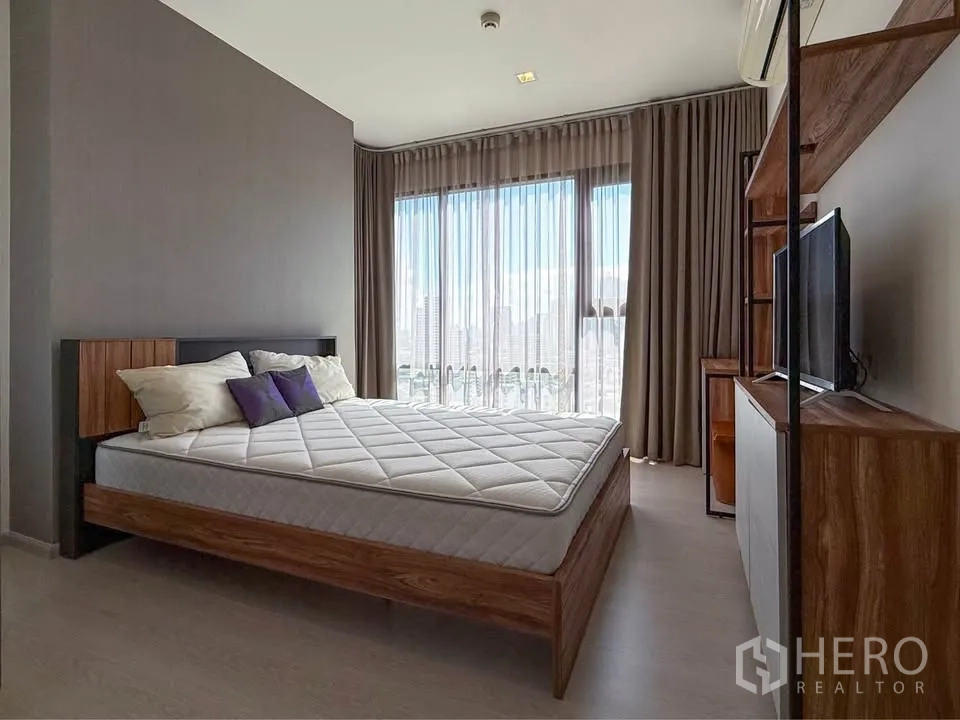 Condominium for rent in Khlong Toei, Bangkok - Spacious room featuring bed, TV unit and panoramic windows with sheer drapes.
