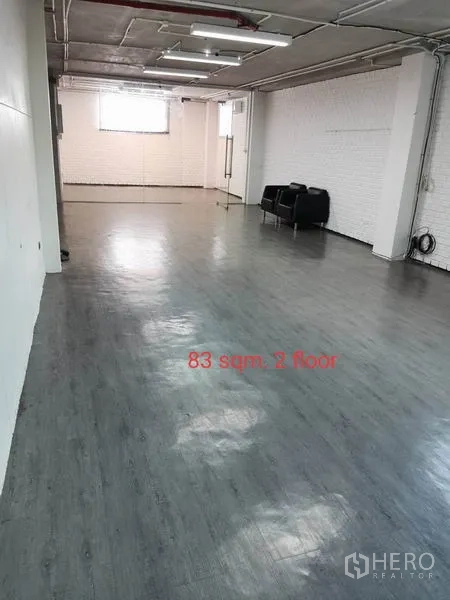 Office Space for rent in Khlong Toei, Bangkok - Long rectangular office floor with window, white brick accent wall, exposed ceiling lighting and two black lounge chairs at the far end.
