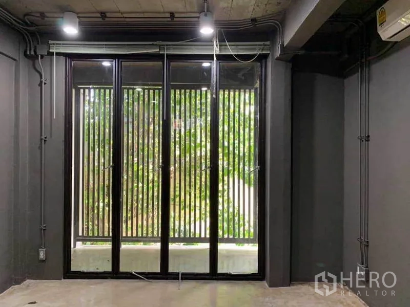 สำนักงานที่บ้าน ให้เช่าในHuai Khwang, Bangkok - มุมมองภายในสู่หน้าต่างกรอบดำสูงพร้อมซี่ระแนงและต้นไม้ภายนอก.