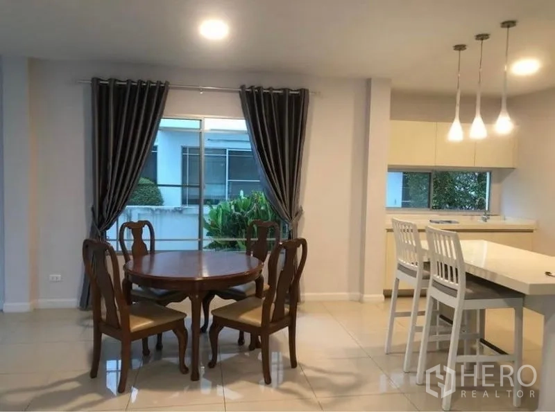 Detached House for rent in Prawet, Bangkok - Dining area with wooden round table beside a breakfast bar and pendant lights.