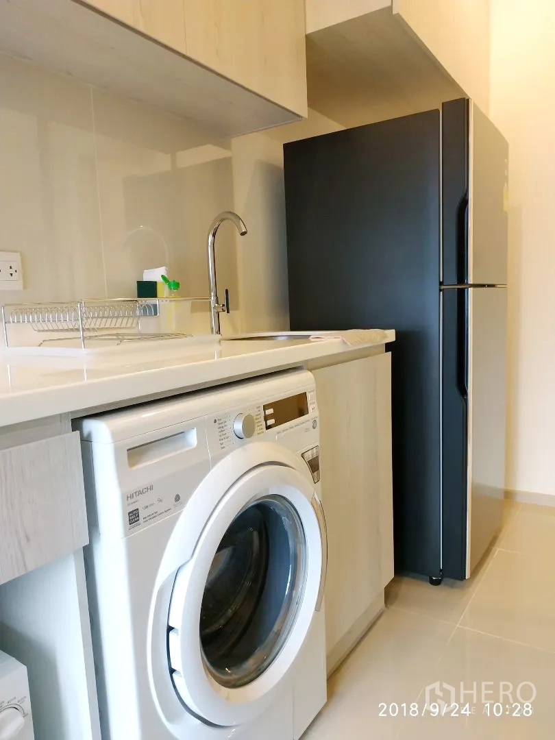Condominium for rent in Huai Khwang, Bangkok - Compact kitchenette with sink, overhead cabinets, front-load washing machine and two-door refrigerator.