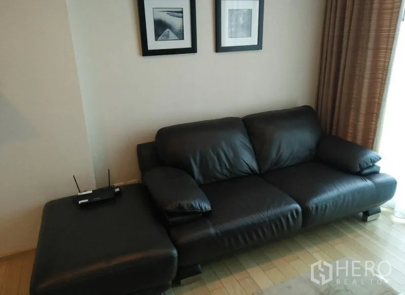 คอนโด ให้เช่าในKhlong Toei, Bangkok - ห้องนั่งเล่นพร้อมโซฟาหนังสีดำ ภาพแขวนผนัง และผ้าม่านสูง