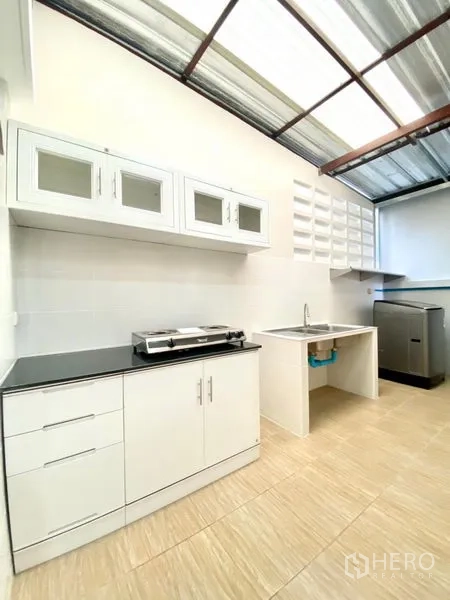 联排别墅 出租在Prawet, Bangkok - 泰式厨房，白色橱柜、黑色台面、水槽与灶台，带遮雨棚。