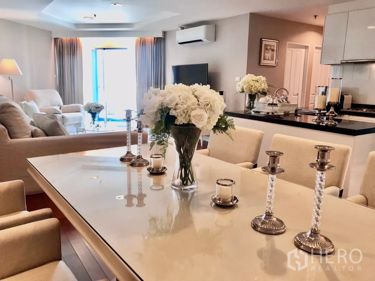 Condominium for rent in Huai Khwang, Bangkok - Modern dining table with upholstered chairs, floral centerpiece and view toward a sunlit balcony.