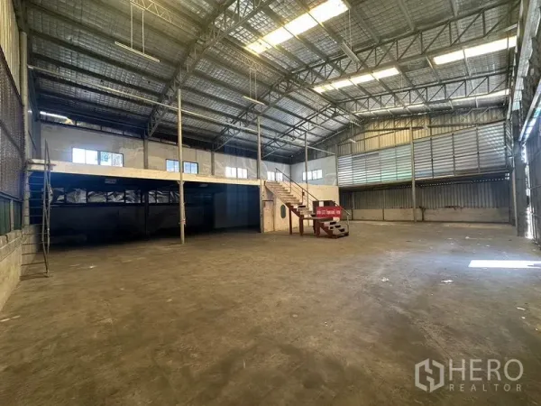 Warehouse for rent in Suan Luang, Bangkok - Spacious warehouse interior with high steel truss roof, skylights, and a mezzanine accessed by stairs.