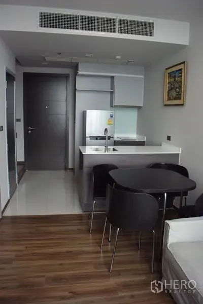 Condominium for rent in Watthana, Bangkok - Open-plan kitchen with breakfast island, round dining table and wood floors in an Ekkamai condo.