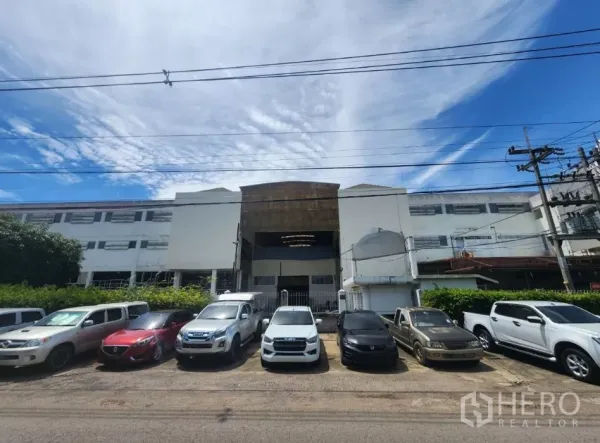 工厂 出租在Mueang Samut Sakhon, Samut Sakhon - 多层工厂正面街景，带大门入口和路边停车，蓝天之下。