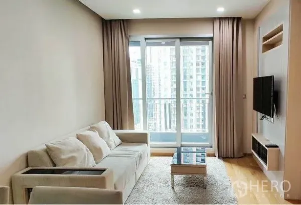 คอนโด ให้เช่าในRatchathewi, Bangkok - ห้องนั่งเล่นสว่าง โซฟาสีอ่อน ทีวีติดผนัง หน้าต่างเต็มบานพร้อมระเบียงวิวเมือง