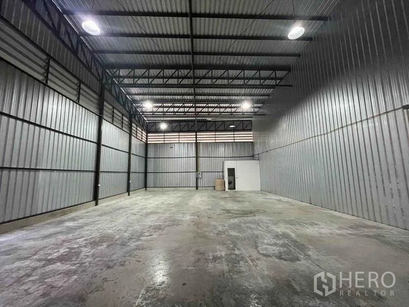 Warehouse for rent in Bang Phli, Samut Prakan - Open storage hall with concrete floor, steel trusses and a small utility room at the rear.