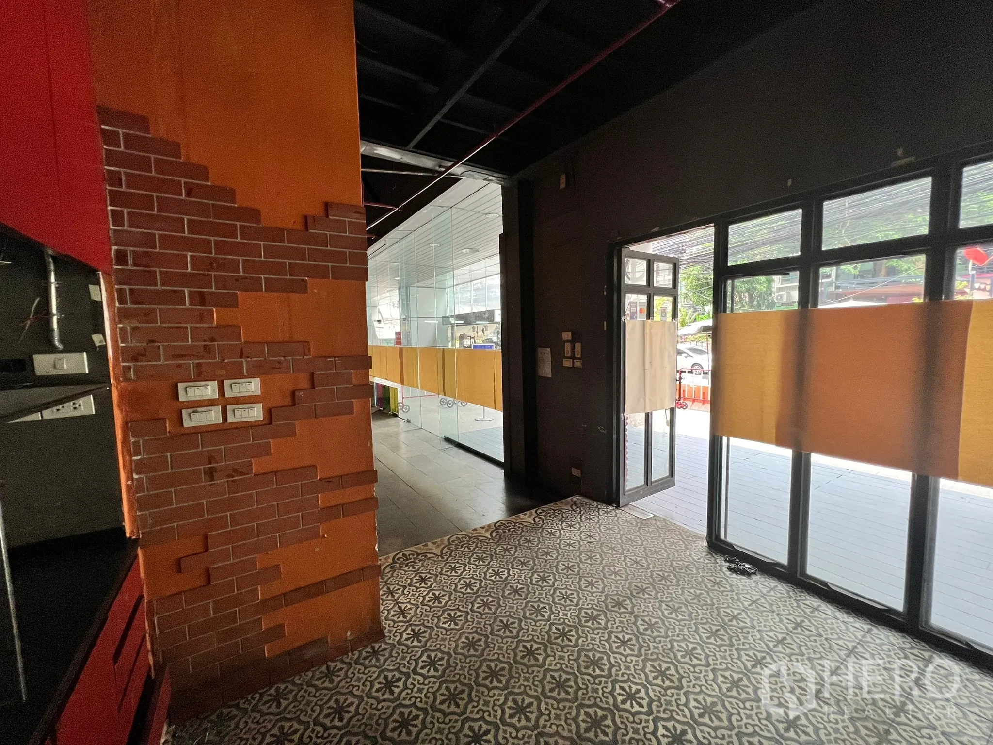 零售空间 出租在Watthana, Bangkok - 入口转角配橙色砖饰、花纹地砖与双扇玻璃门。