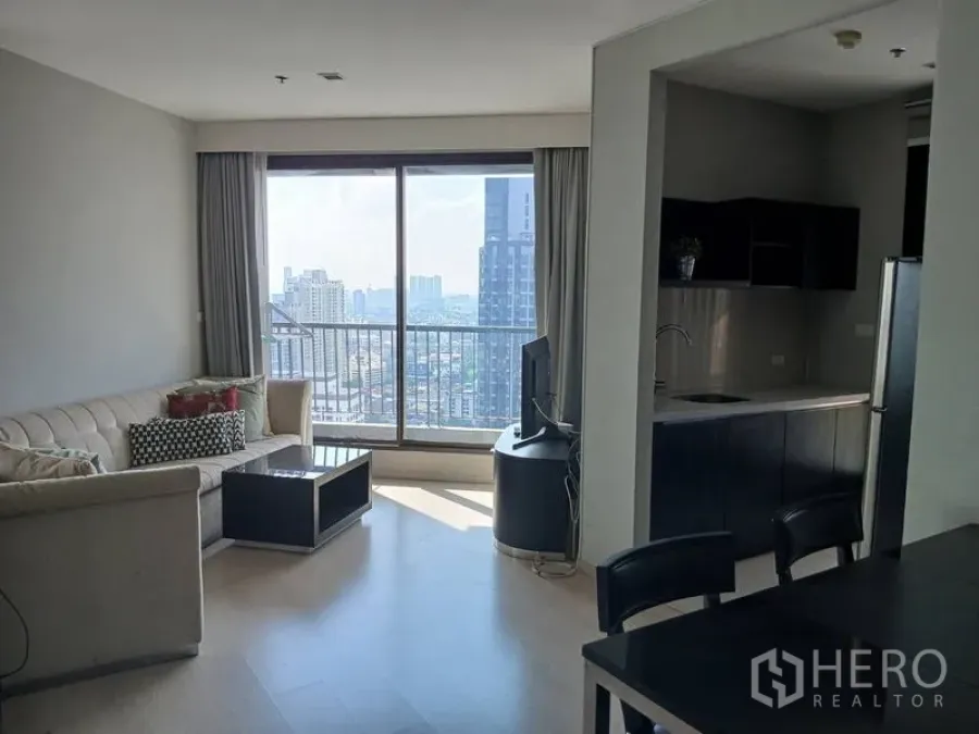 คอนโด ให้เช่า - มุมมองอีกด้านของห้องนั่งเล่น เปิดสู่ระเบียงและครัวขนาดกะทัดรัดพร้อมวิวเมือง