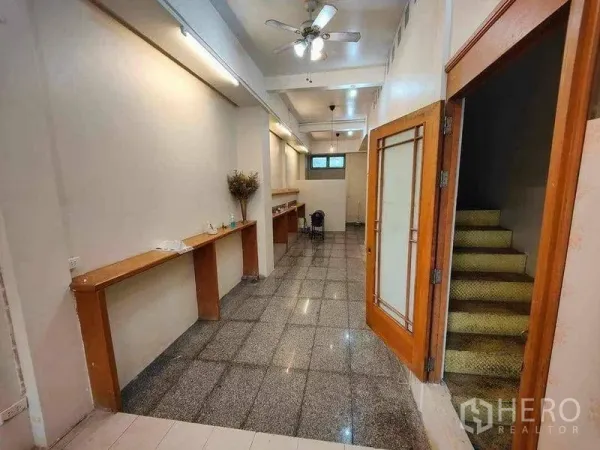 零售空间 出租在Khlong Toei, Bangkok - 狭长店内，花岗岩地面、木质操作台，玻璃门后为楼梯。