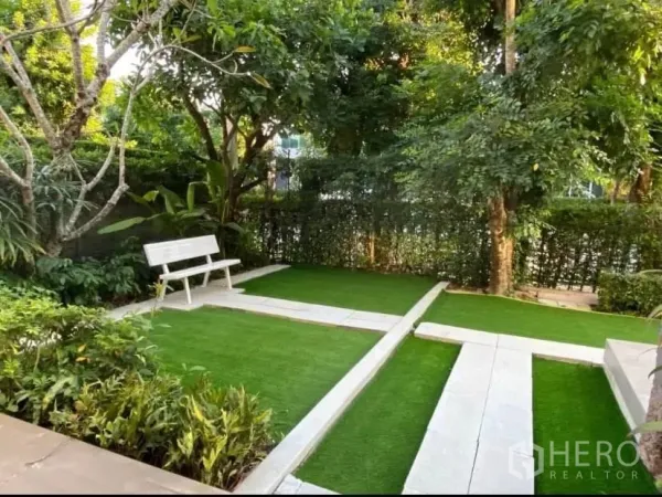 独立式住宅 出租或出售在Prawet, Bangkok - 花园一角，绿篱与乔木，白色长椅置于草坪上。