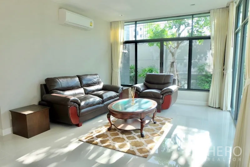 บ้าน ให้เช่าในPrawet, Bangkok - ห้องนั่งเล่นสว่าง โซฟาหนัง โต๊ะกลาง และผนังกระจกเห็นสวน