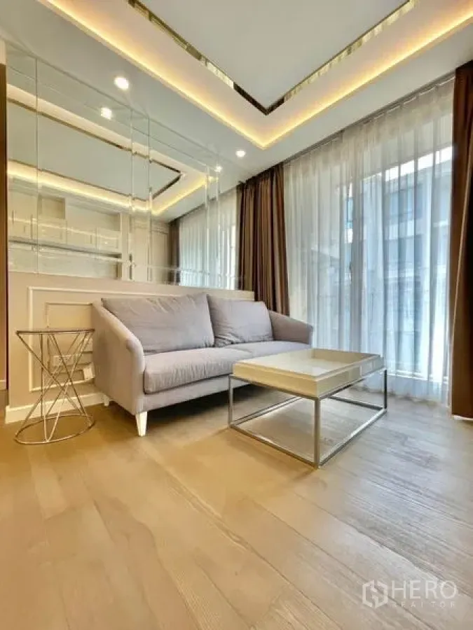 Condominium for sale in Huai Khwang, Bangkok - Bright living room with sofa, coffee table, mirrored wall and floor-to-ceiling curtains in a Bangkok condo.