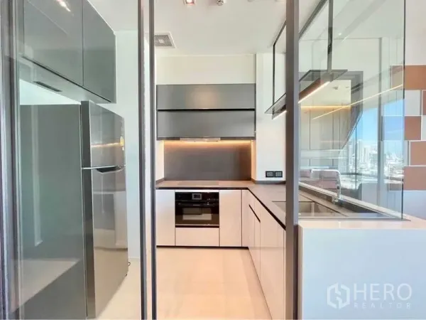 Condominium for rent in Watthana, Bangkok - Enclosed modern kitchen with built-in oven, upper cabinets and stainless refrigerator overlooking the city.