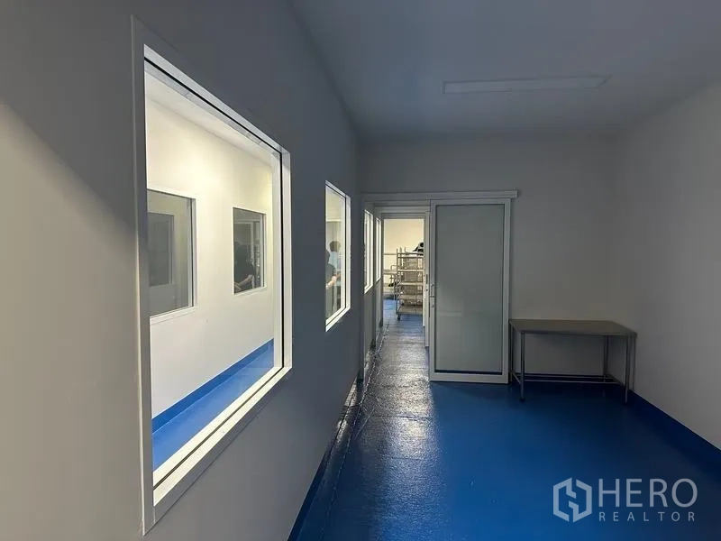 Warehouse for rent in Pak Kret, Nonthaburi - Hygienic corridor with observation windows and a sliding door beside a stainless work table.