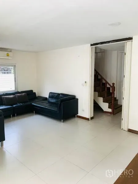 联排别墅 出租或出售在Huai Khwang, Bangkok - 明亮客厅，白色地砖、黑色皮沙发与木楼梯