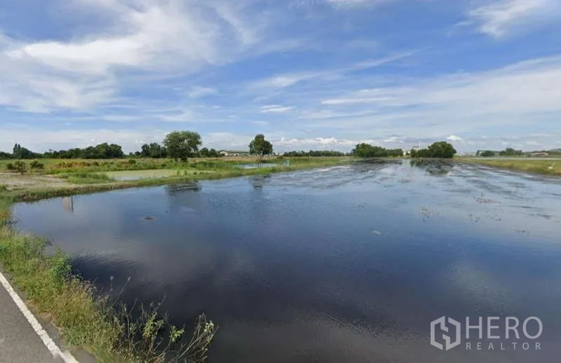 Land for sale in Chachoengsao - Large reflective pond bordered by grass and fields with a roadside edge visible.