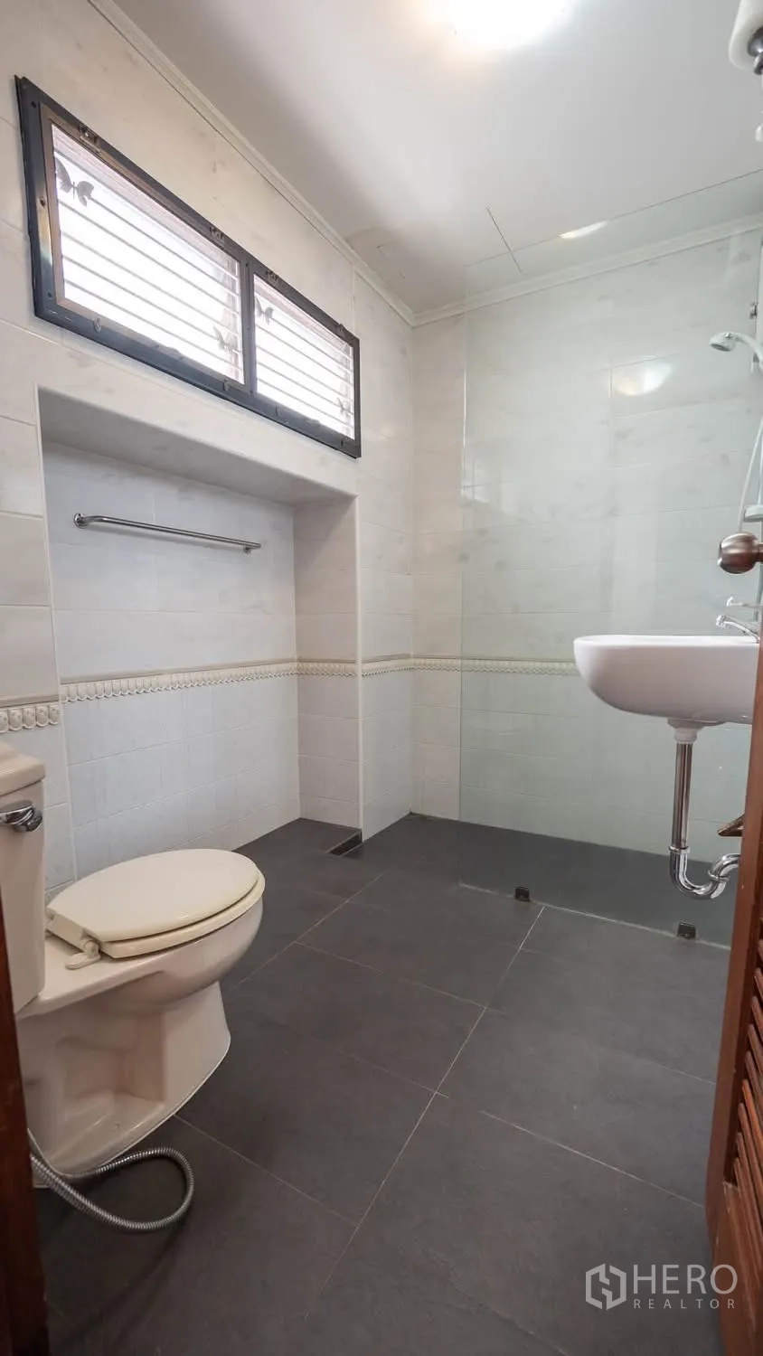 Townhouse for rent in Watthana, Bangkok - Bathroom with gray floor tiles, open shower area, toilet, and wall-hung basin.