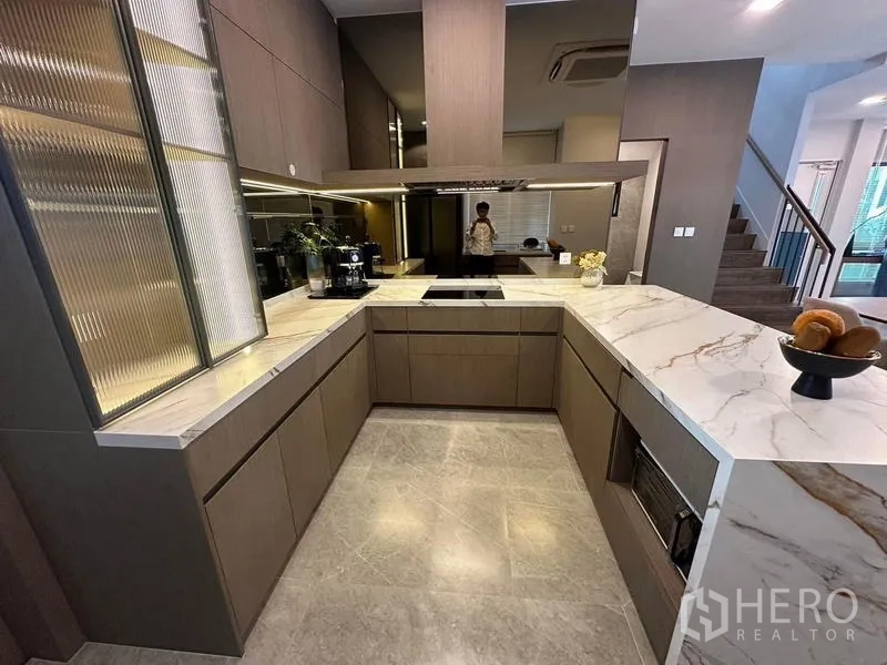 Detached House for rent in Samut Prakan - U-shaped kitchen with marble countertops, induction hob and ample storage.
