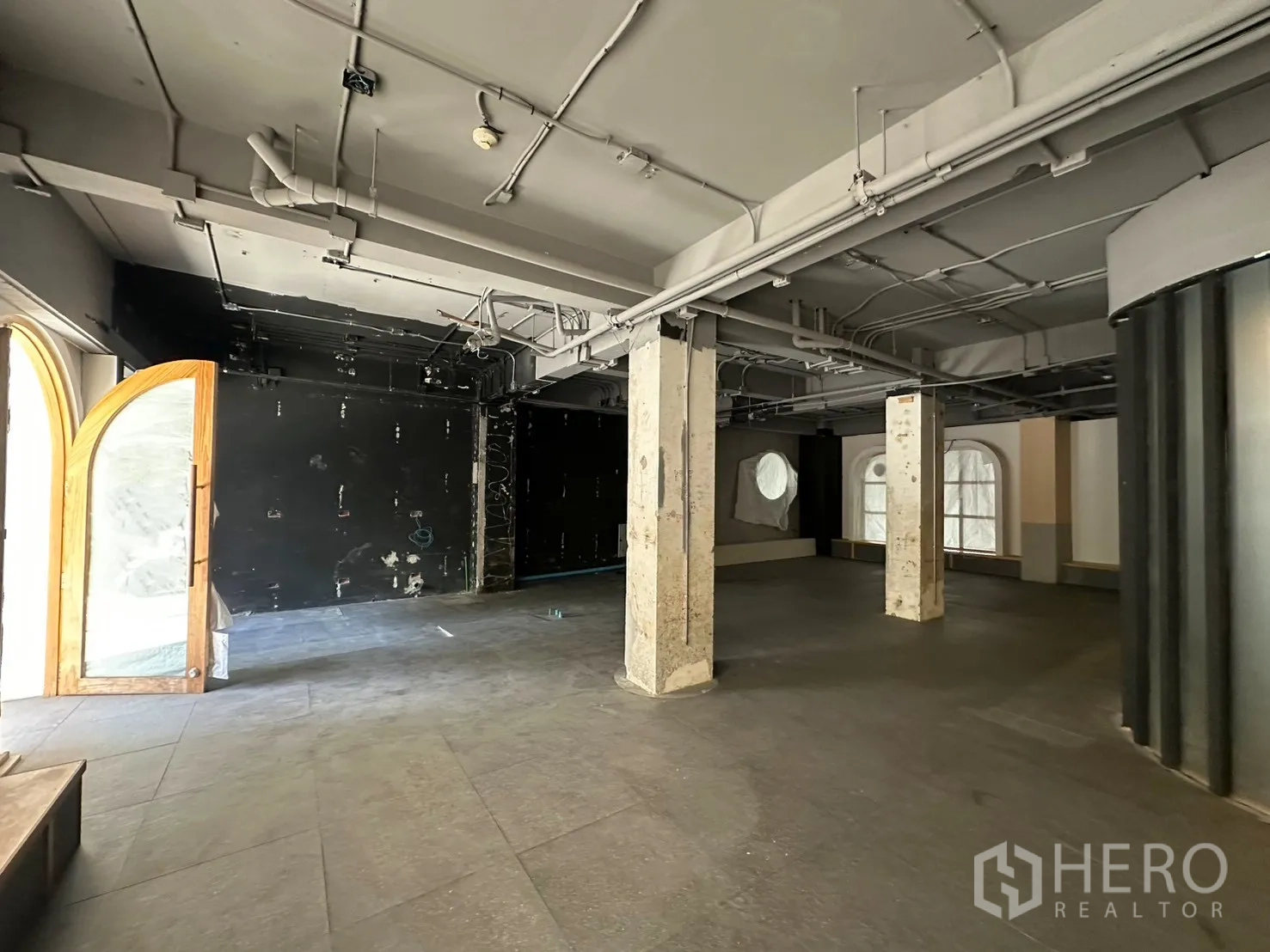 Retail Space for rent in Watthana, Bangkok - Large open area with concrete columns, a black feature wall, and an arched wooden-framed door.