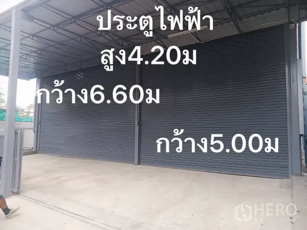 Warehouse for rent in Huai Khwang, Bangkok - Two large electric roller shutter doors beneath a metal awning at the warehouse front.