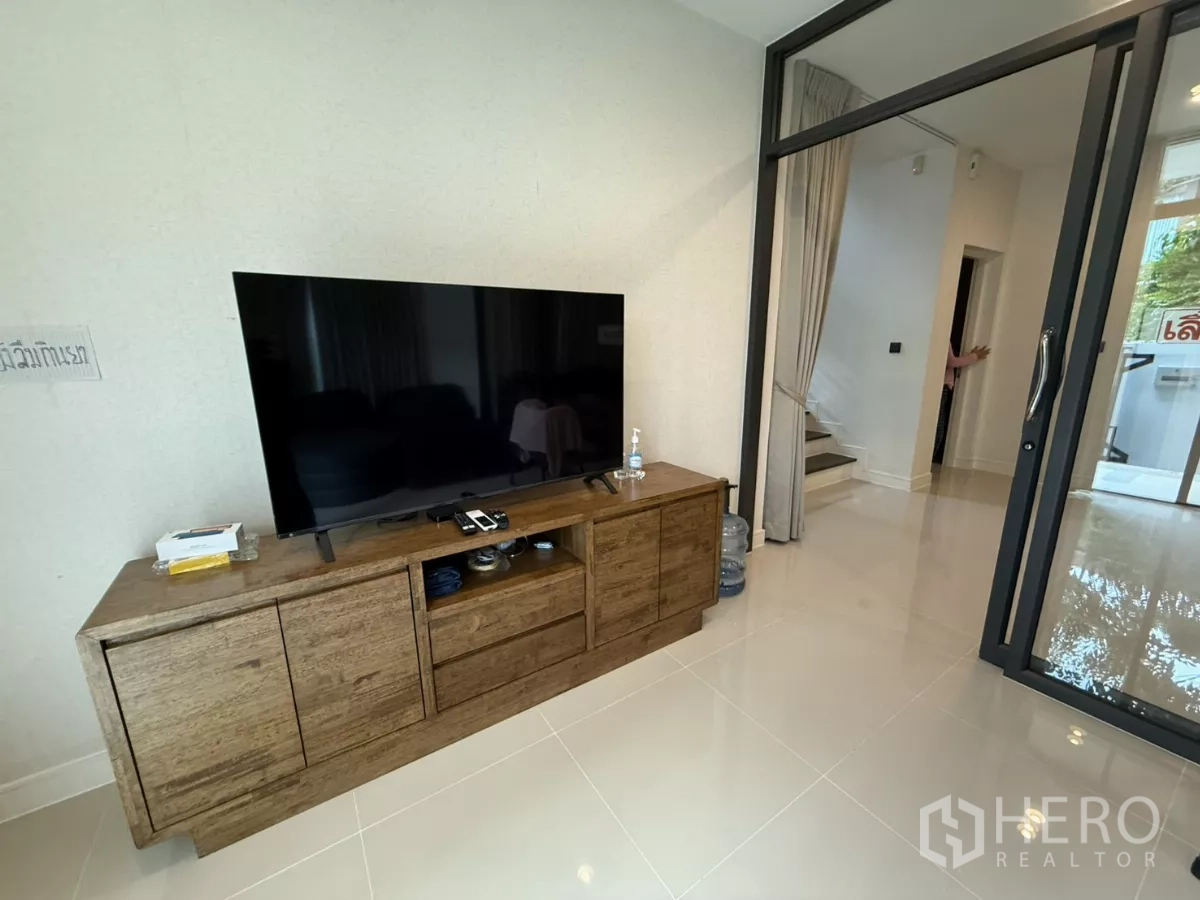 บ้าน ให้เช่าในBang Kapi, Bangkok - มุมห้องนั่งเล่นมีตู้ทีวี ประตูกระจก และบันไดขึ้นชั้นบน