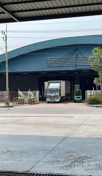 货栈 出租在Si Racha, Chon Buri - 蓝色屋顶仓库的遮雨装卸区，卡车与叉车正在月台作业