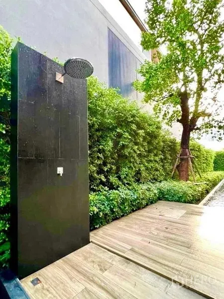 บ้าน ขายในHuai Khwang, Bangkok - ฝักบัวกลางแจ้งแผงสีดำข้างระเบียงไม้ ล้อมด้วยพุ่มไม้เขียว