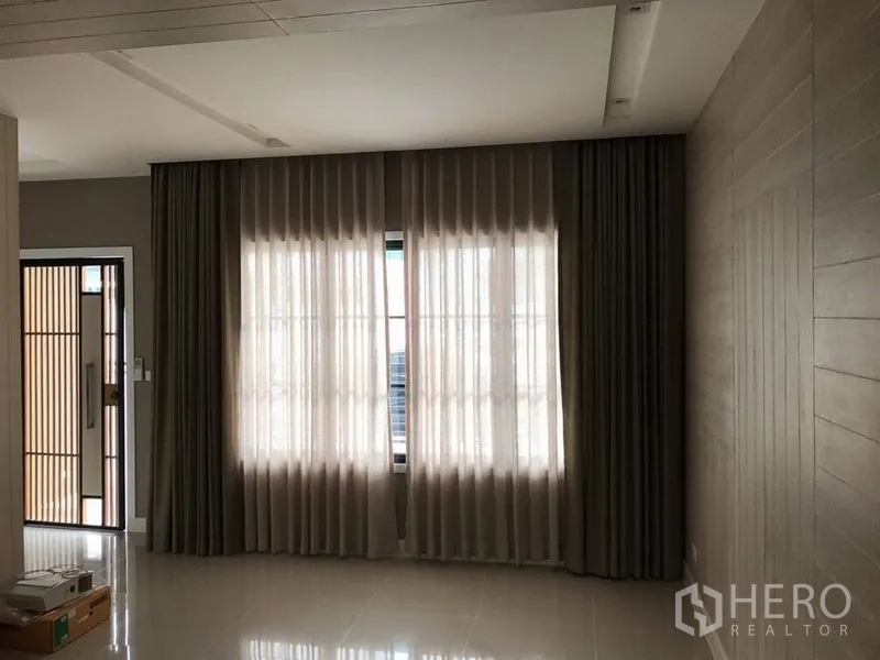 Townhouse for rent - Living area with full-length sheer curtains, recessed ceiling, and neutral wood paneling.