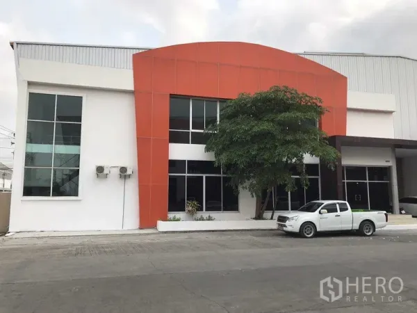 工厂 出租在Samut Prakan - 现代化工厂外立面，橙色门头与两层玻璃办公室及车道。