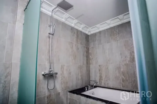 Condominium for rent or sale in Khlong Toei, Bangkok - Modern bathroom with soaking bathtub and rain shower, tiled walls and decorative cornice.
