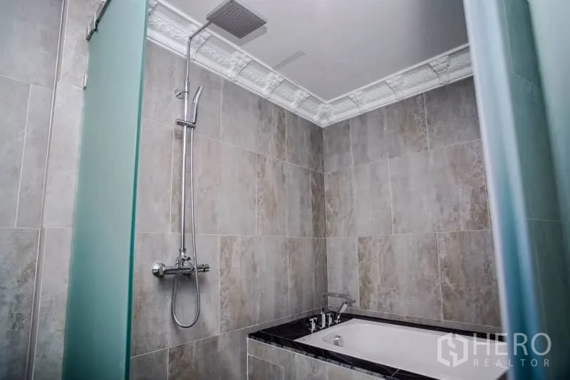 Condominium for rent or sale in Khlong Toei, Bangkok - Modern bathroom with soaking bathtub and rain shower, tiled walls and decorative cornice.