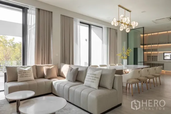 Detached House for rent in Saphan Sung, Bangkok - Sunlit living room with L-shaped sofa, floor-to-ceiling windows, and adjoining dining zone.
