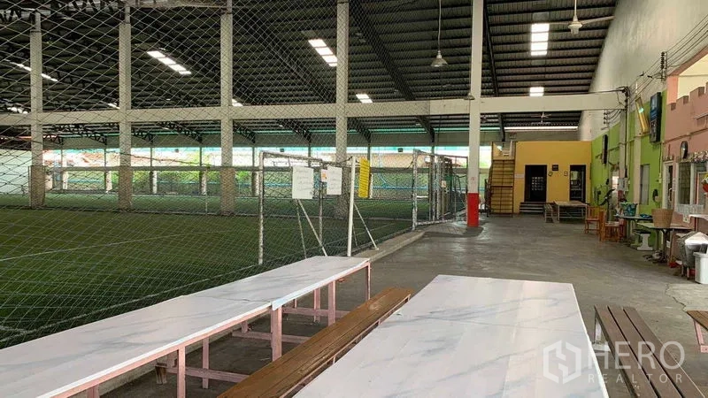 Warehouse for rent in Phra Pradaeng, Samut Prakan - Canteen seating area beside a netted indoor pitch under a metal roof.