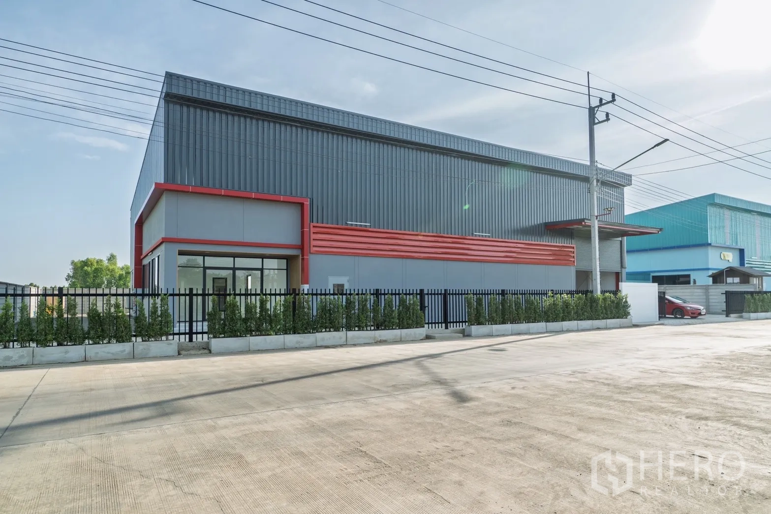 โรงงาน for rent or sale in Lam Luk Ka, Pathum Thani - ด้านหน้าโรงงานสมัยใหม่ผนังเมทัลชีทกรอบสีแดง รั้วรอบและลานคอนกรีตกว้าง