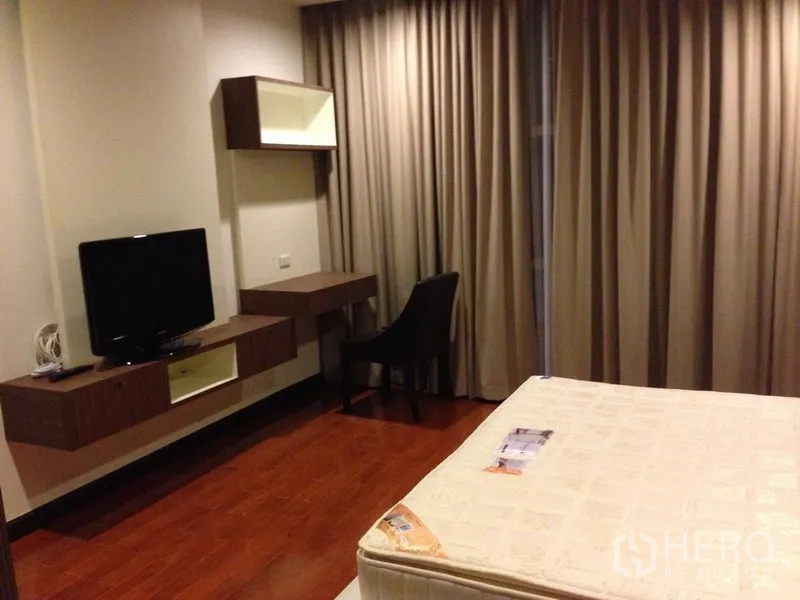 คอนโด ให้เช่าในWatthana, Bangkok - ห้องนอนมีทีวีติดผนัง โต๊ะทำงาน และผ้าม่านสูงจรดพื้นบนพื้นไม้โทนอุ่น