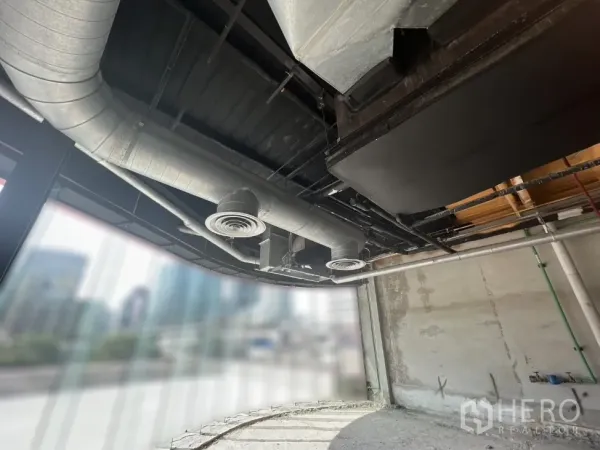 零售空间 出租在Pathum Wan, Bangkok - 弧形玻璃店面与金属风管，窗外可见城市景观。